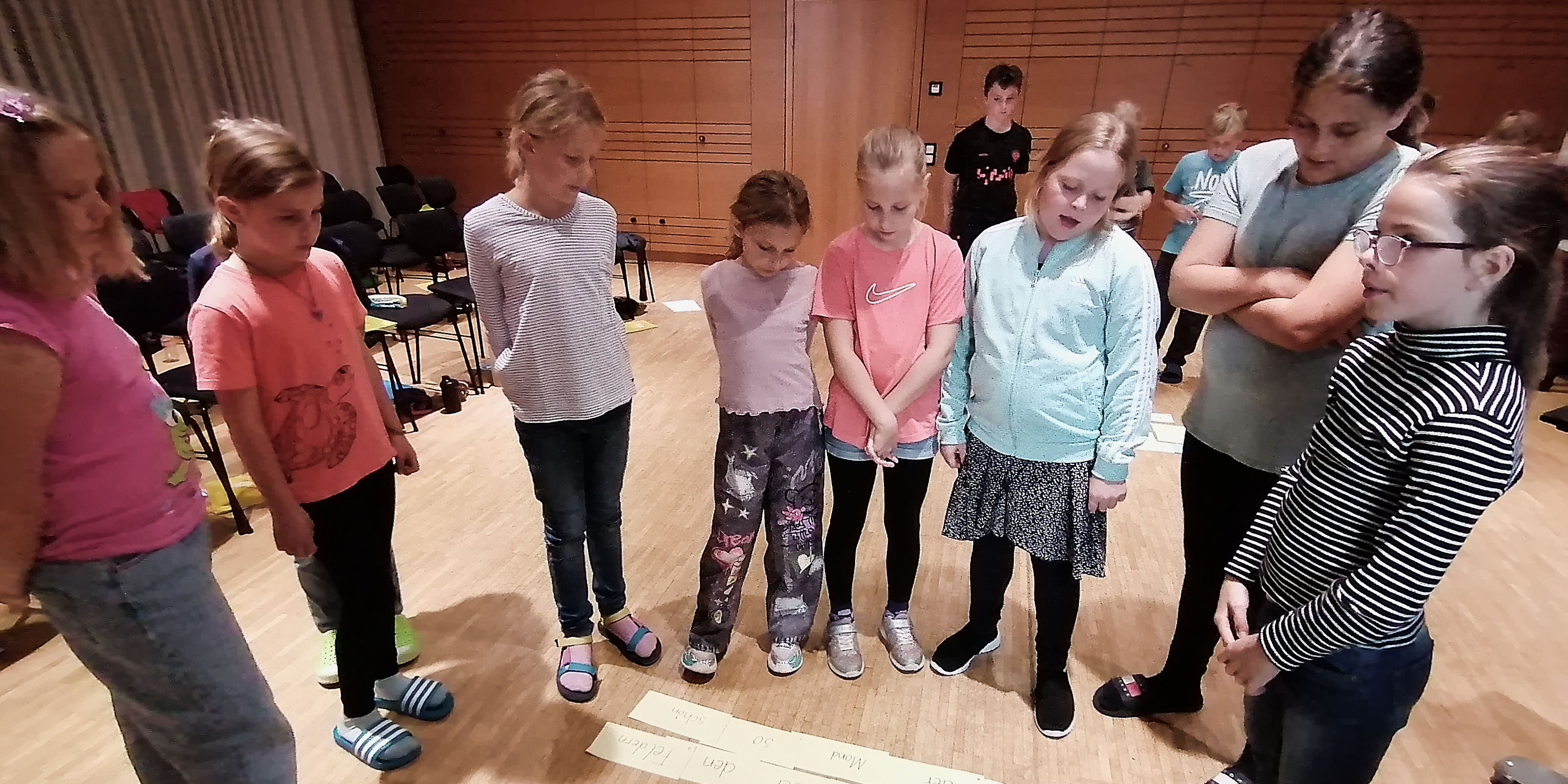 Mehrere Kinder stehen im Halbkreis und schauen auf mehrere am Boden liegende Blätter